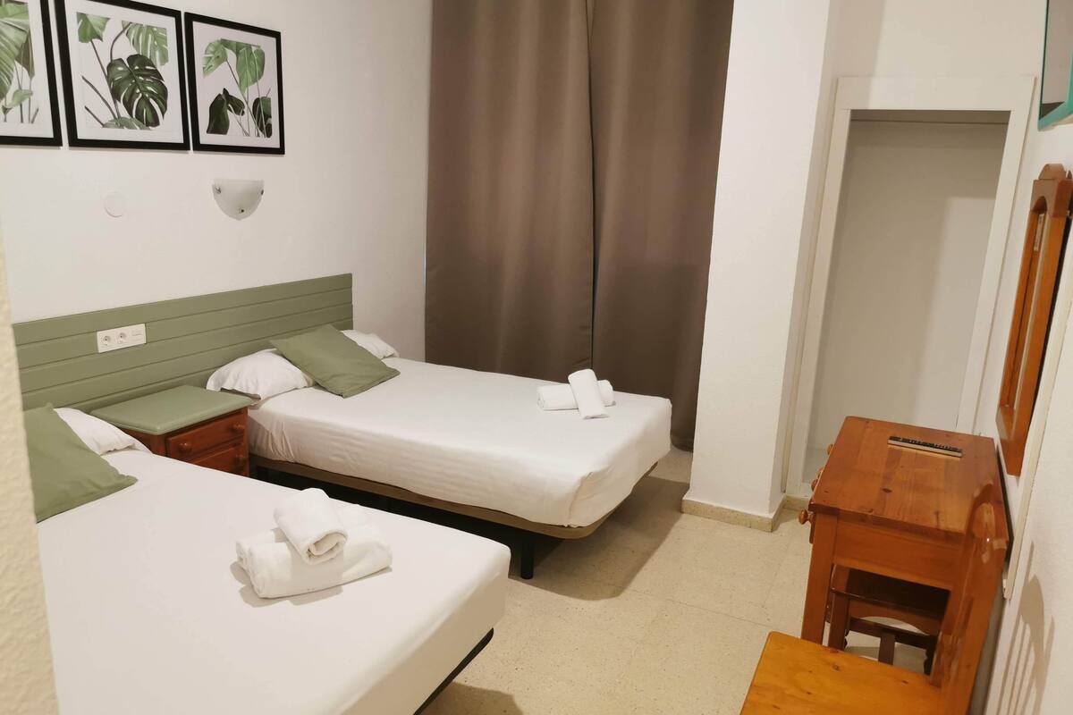 Ein Hotelzimmer mit zwei Einzelbetten, einem kleinen Holztisch und einer wandmontierten Lampe.