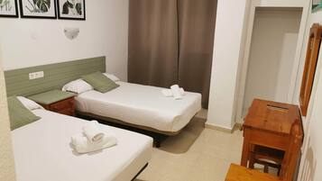 Habitación de hotel con dos camas individuales, una mesita de madera y una lámpara fijada a la pared.