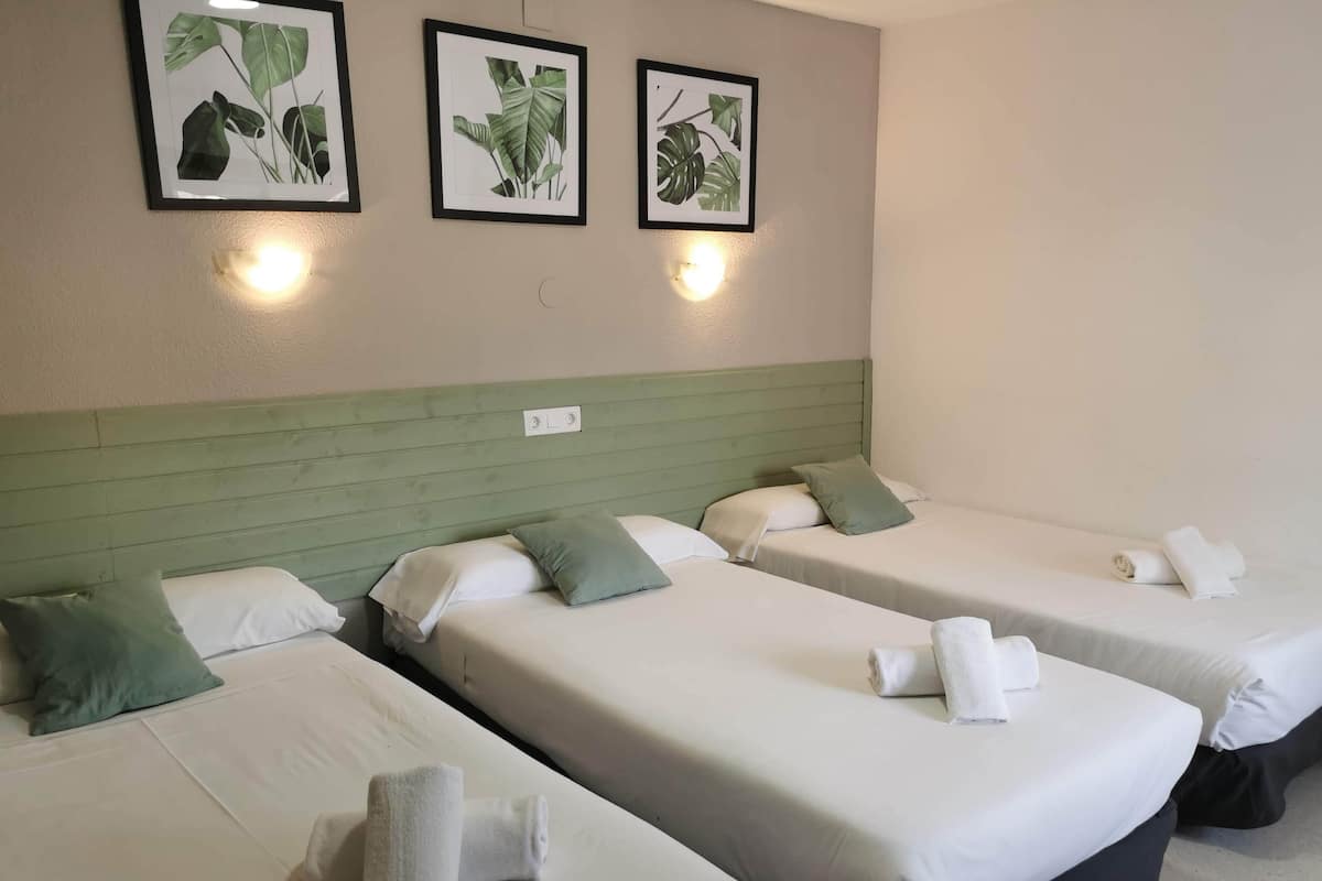 Ein Hotelzimmer mit drei Einzelbetten, jeweils mit weißer Bettwäsche und grünen Kissen. An der Wand über den Betten befinden sich gerahmte Pflanzenbilder.