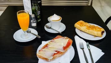Ein Tisch mit einem Glas Orangensaft, einer Tasse Kaffee, einem Gebäck und einem Sandwich.