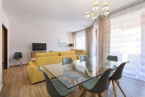 A modern living room with a glass dining table, yellow sofa, and a TV.