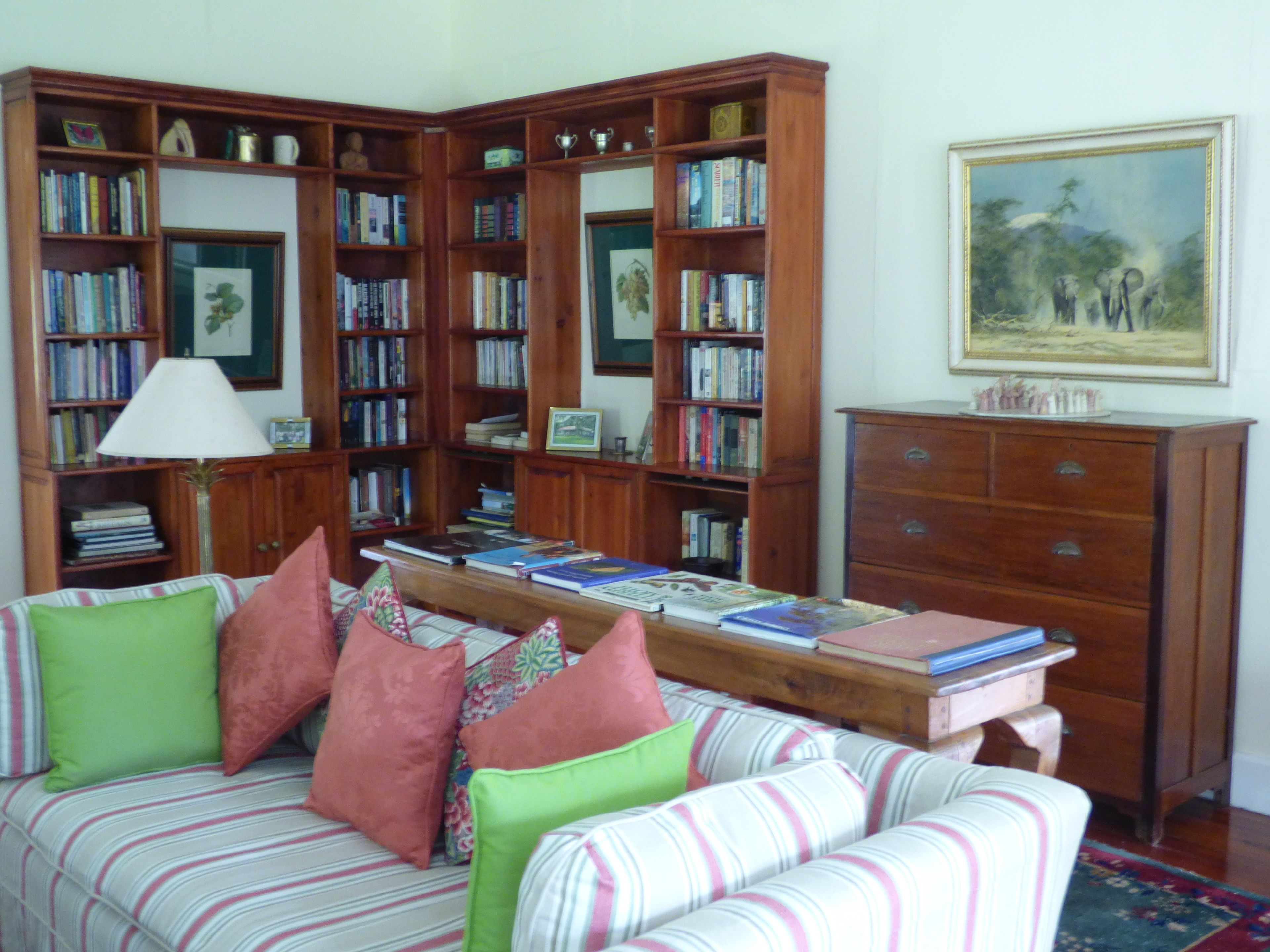 A cozy living room with a striped sofa, a wooden coffee table with books, and a bookshelf filled with books and decorative items.