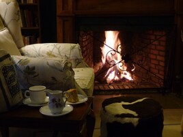A cozy room with a fireplace, a sofa, a table with a teapot and a cup, and a decorative pillow.