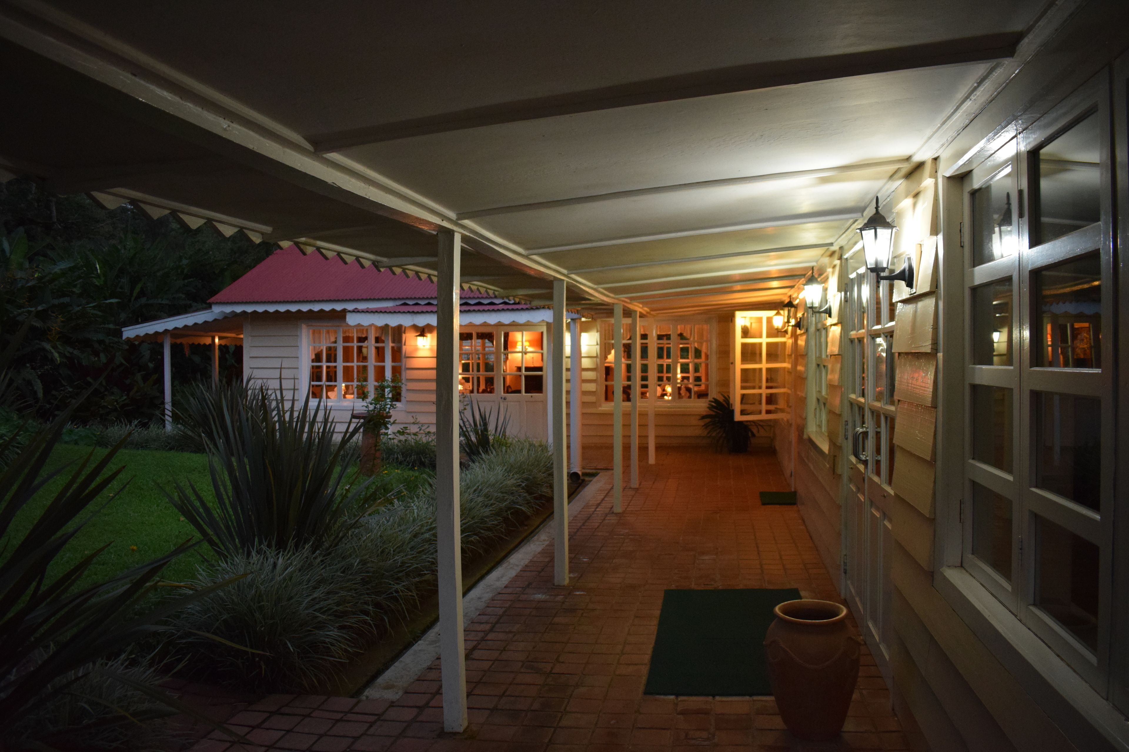 A covered outdoor corridor with a red-roofed building on the left, a brick pathway, and a green mat at the entrance.