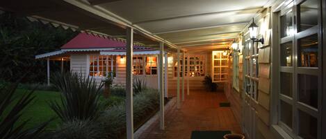 A covered outdoor corridor with a red-roofed building on the left, a brick pathway, and a green mat at the entrance.