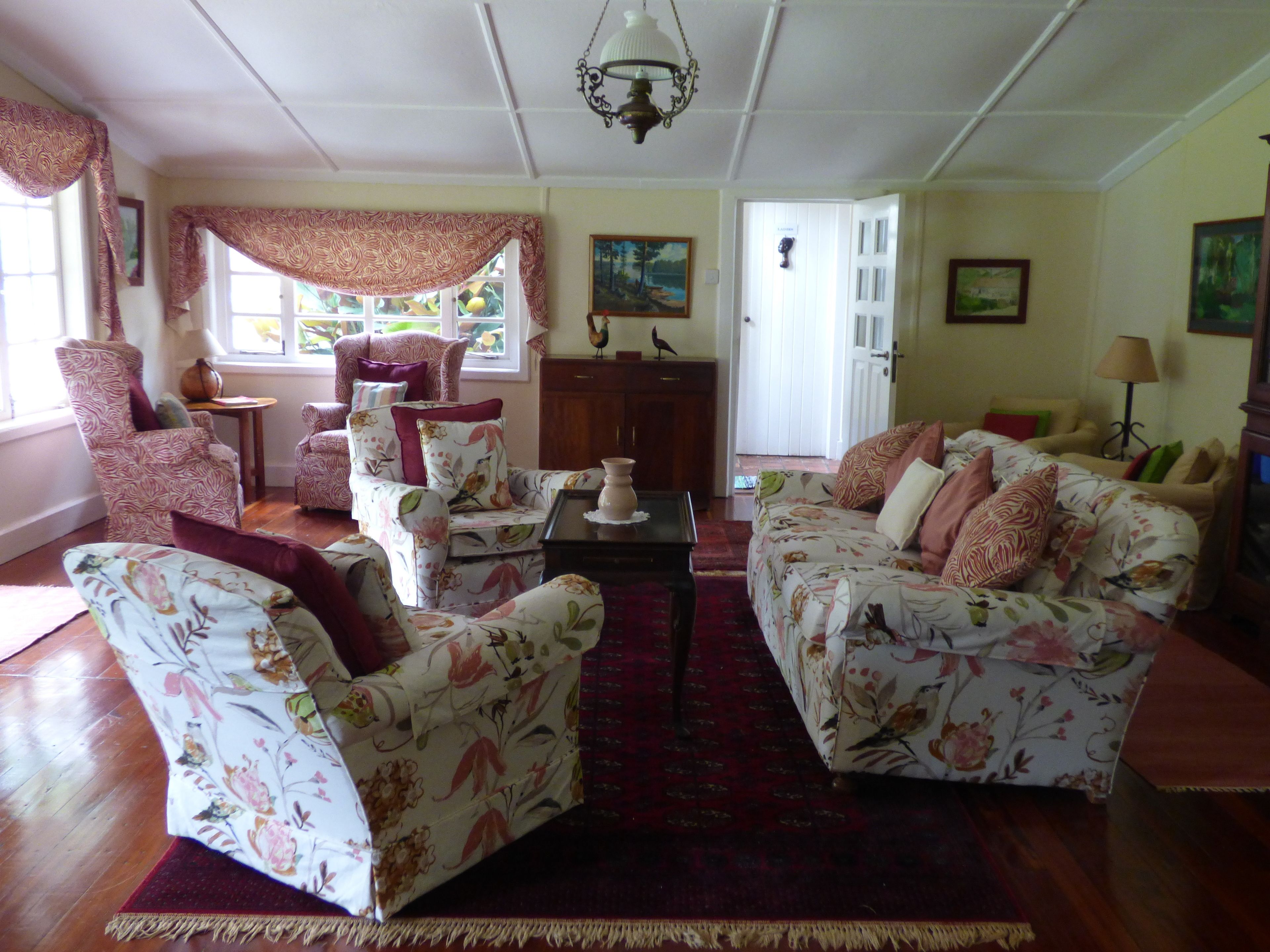 A living room with floral-patterned furniture, a chandelier, and a view of the outdoors through large windows.