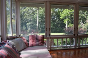 A room with a large window, a wooden floor, and a bed with striped bedding.