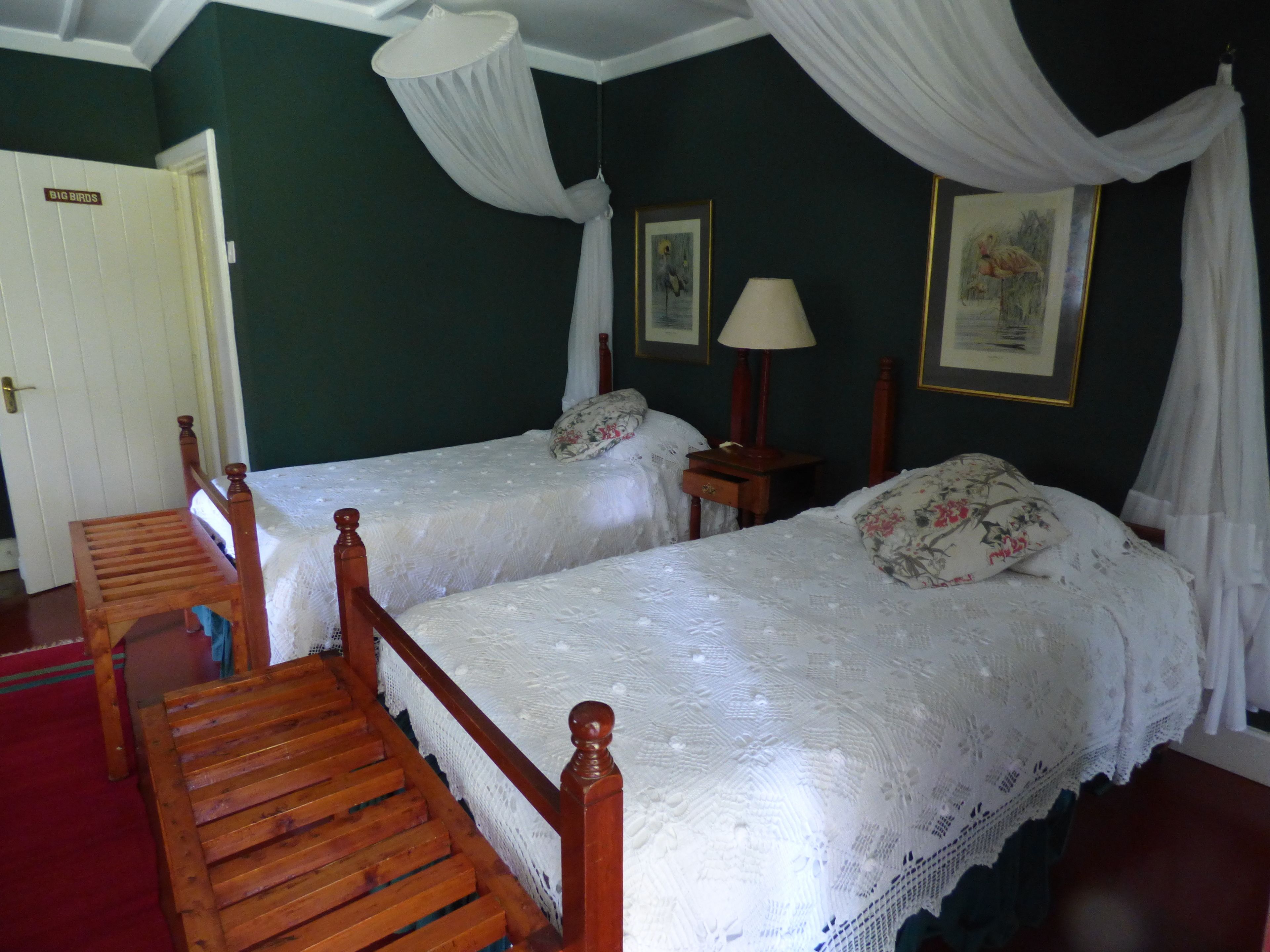 A bedroom with two wooden beds, a nightstand, a lamp, and a door labeled "BIG BIRDS".