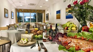 Comedor con mesas dispuestas para una comida, que presenta una variedad de frutas, verduras y un centro de mesa con pescado.