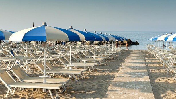Una playa con filas de tumbonas y sombrillas azules y blancas.