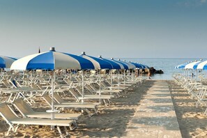 A beach with rows of sun loungers and blue and white umbrellas. - Hotel Lina (Misano Adriatico)