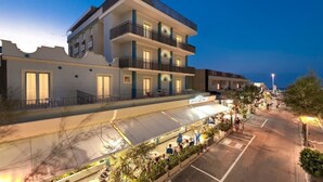 Un hotel de varios pisos con balcones, una zona de estar al aire libre techada y un estacionamiento.