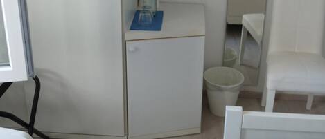 Un dormitorio con una cama, un escritorio pequeño con un jarrón y un libro, una silla y un armario blanco.