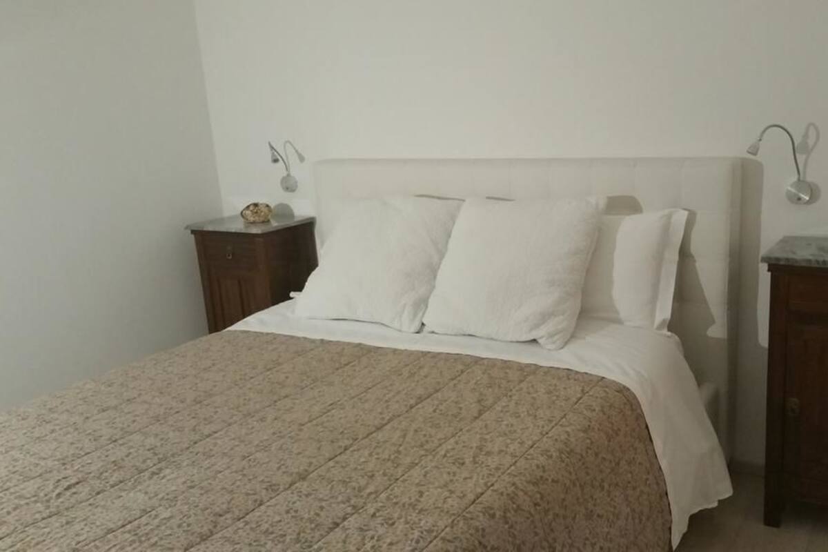 Una cama bien hecha con ropa blanca, un cabecero y dos mesitas de noche con lámparas.