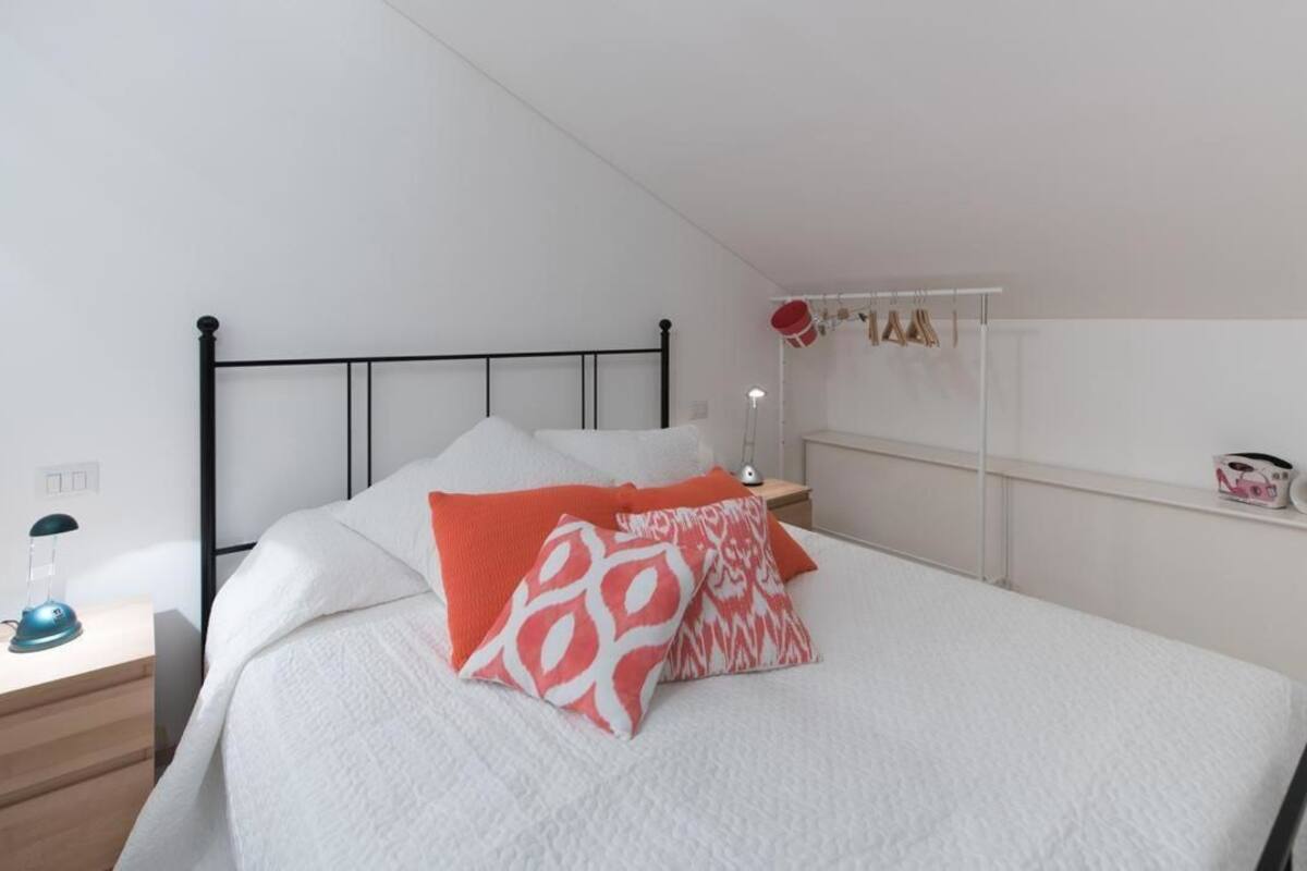 Un dormitorio con una cama, una mesita de noche, una lámpara y una estantería con objetos.