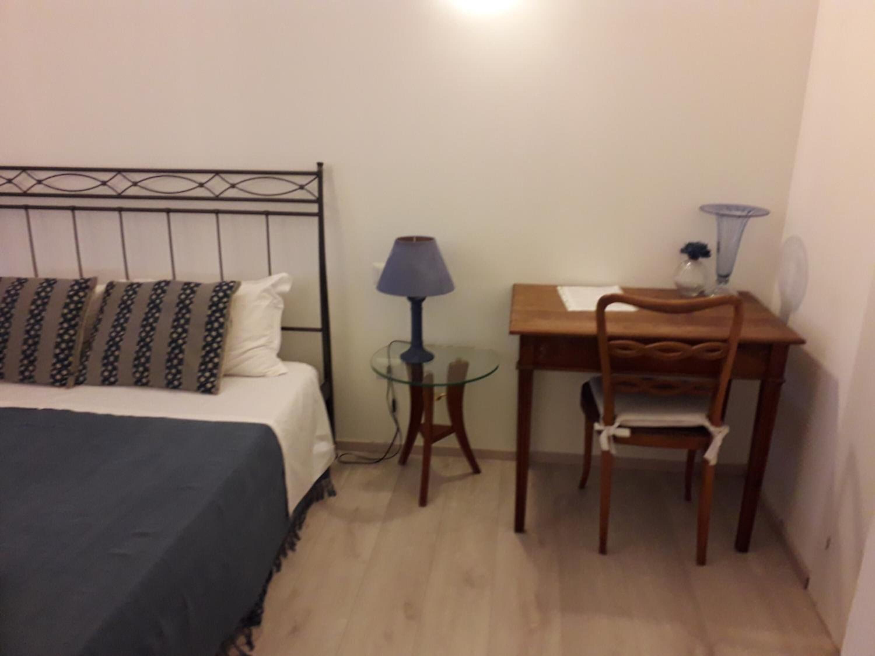 Una habitació petita amb llit, escriptori, cadira i làmpada.