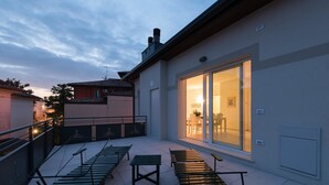 Eine Dachterrasse mit Sitzgelegenheiten im Freien und einer Glastür, die zu einem Innenraum führt.
