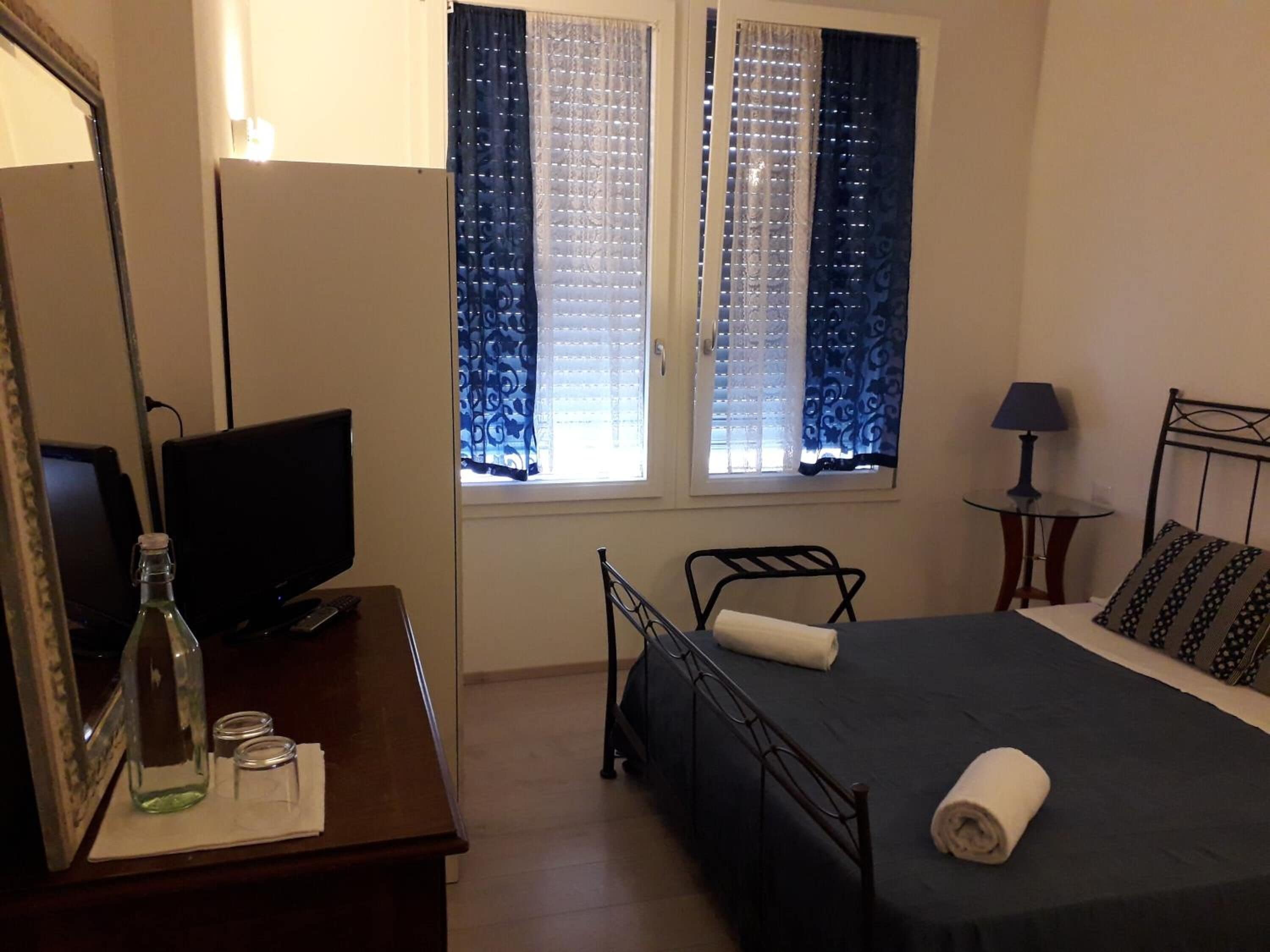 Un dormitorio con cama, escritorio, computadora, espejo y ventana con cortinas.