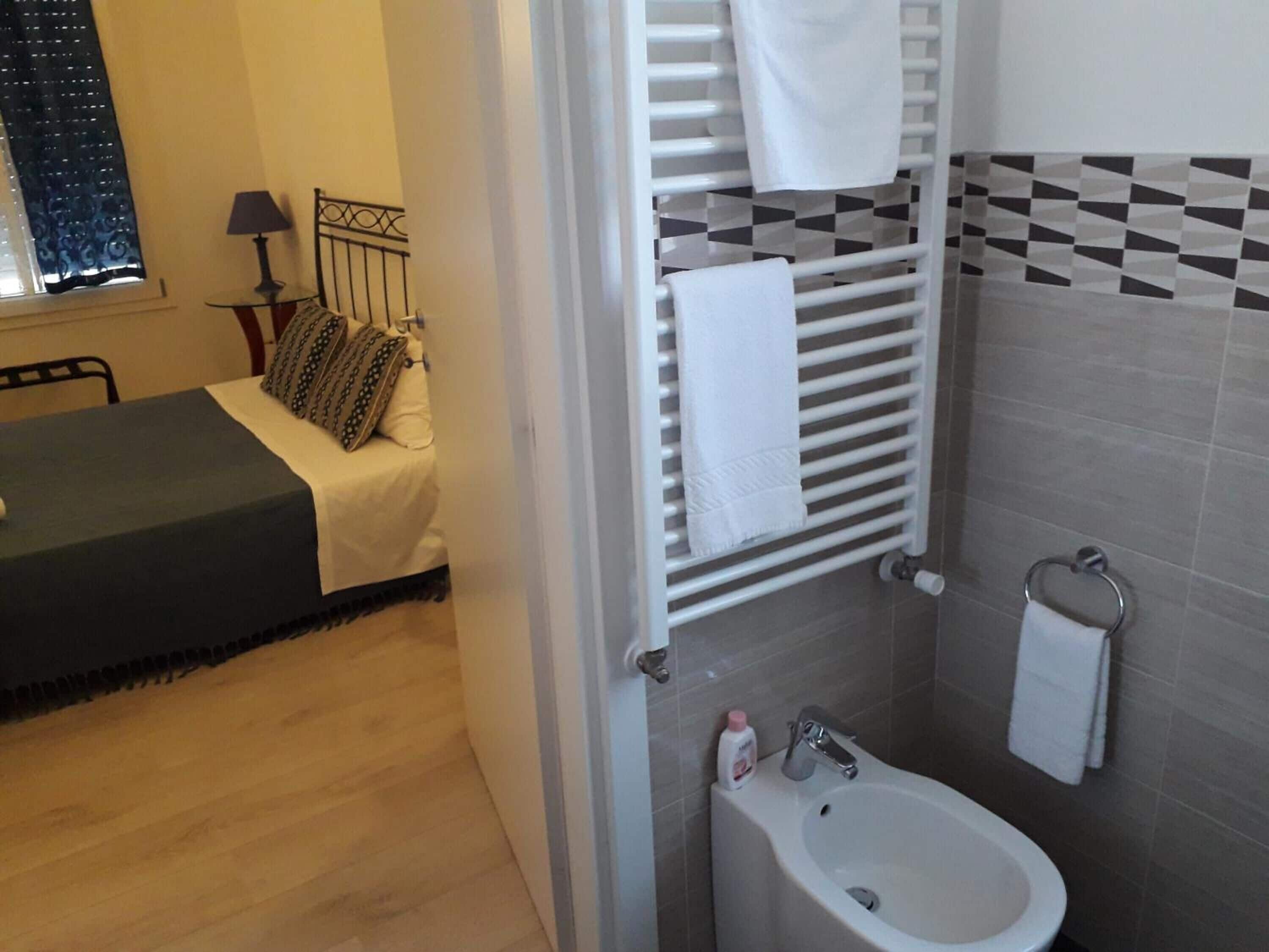 Une chambre à coucher comprenant un lit, une table de chevet, une lampe et une vue sur une salle de bain avec un lavabo et un porte-serviettes.