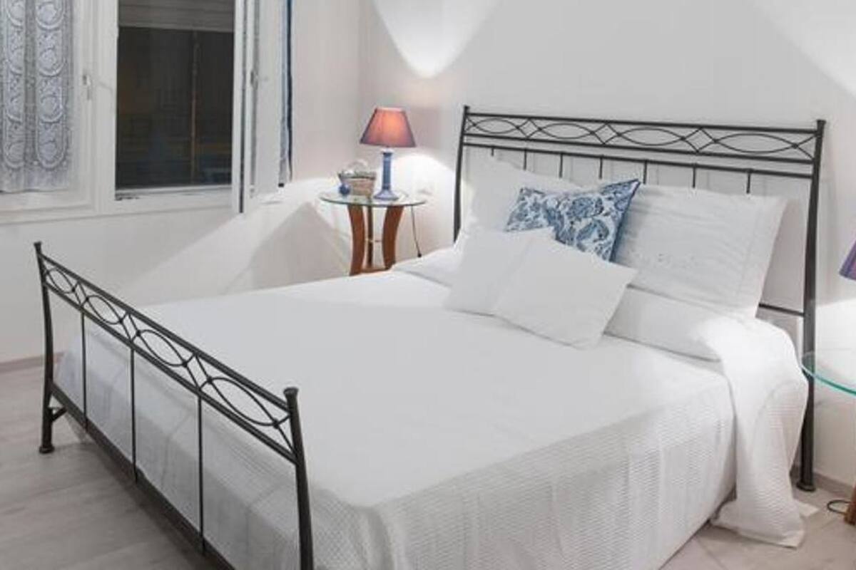 Un dormitorio ordenado con cama, mesitas de noche, lámparas y un jarrón decorativo.