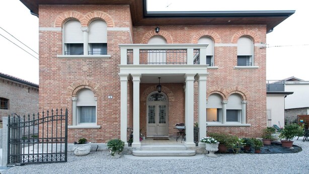 Ein zweistöckiges Backsteinhäuschen mit Balkon, Eingangstür und einem kleinen Garten mit Blumentöpfen.