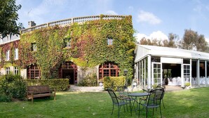 Un bâtiment dont les murs sont recouverts de lierre et qui dispose d’un espace extérieur abrité avec des tables et des chaises.