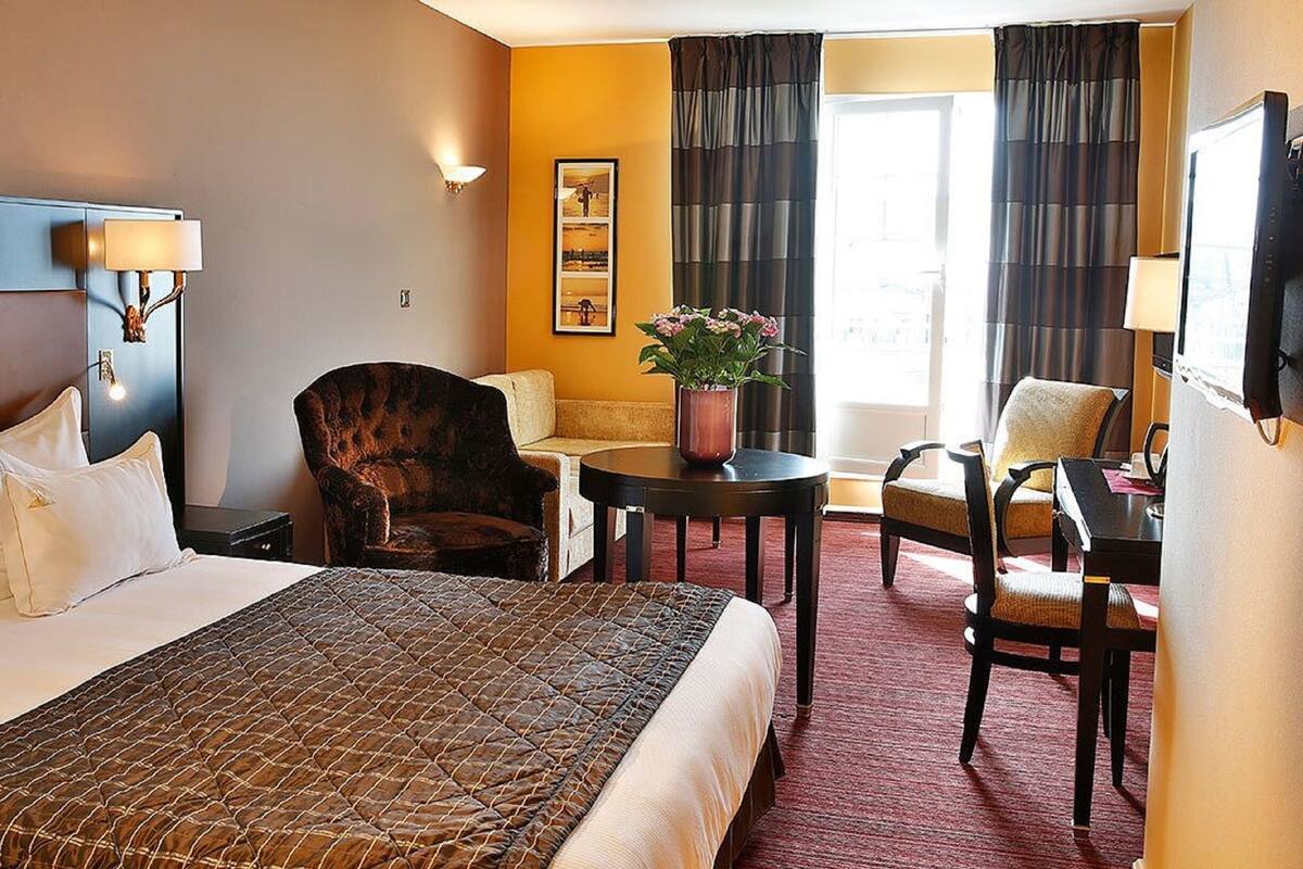 Une chambre d’hôtel avec un grand lit, un bureau, une chaise, un canapé et une petite table sur laquelle est posée une plante en pot.