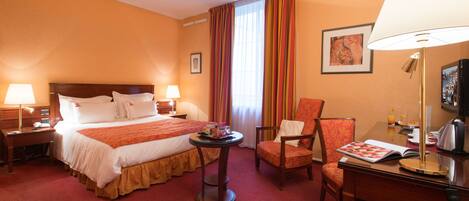 A hotel room with a large bed, two bedside tables, a desk with a chair, a small round table, and a television.