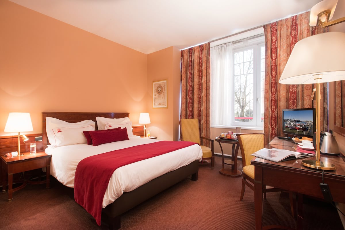 Une chambre d’hôtel avec un grand lit, deux tables de chevet avec des lampes, une chaise, un bureau avec une lampe et un téléviseur.