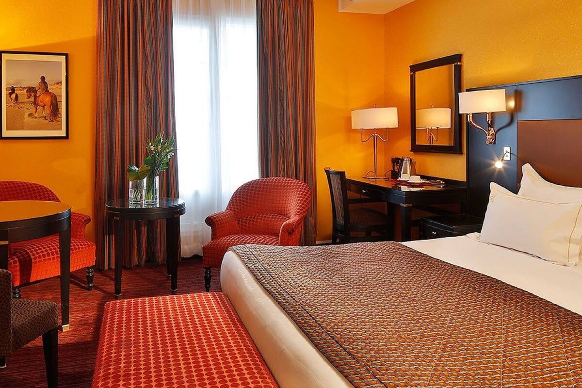 Une chambre d’hôtel avec un grand lit, un bureau, une chaise, une petite table avec un vase et un tableau au mur.