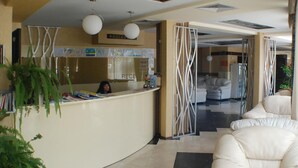 A reception area with a counter, a receptionist, and a waiting area with chairs. - Lotos Hotel (Balchik)
