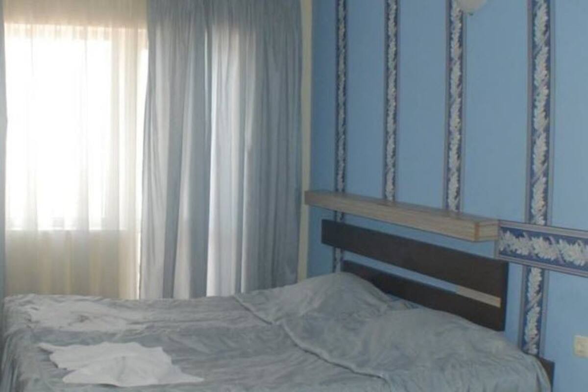 A bedroom with a bed, a television on a stand, and curtains on the window.