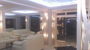 A modern living room with a sectional sofa, a glass door leading outside, and contemporary decor. - Lotos Hotel (Balchik)