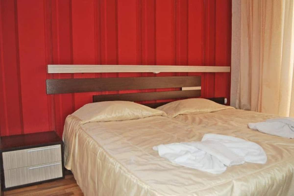 A bed with a wooden headboard, a bedside table, and a red curtain backdrop.