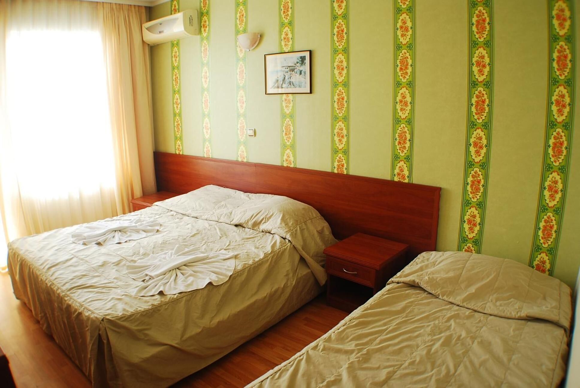 Un dormitorio con dos camas, cabeceros de madera, una mesita de noche y aire acondicionado instalado en la pared.