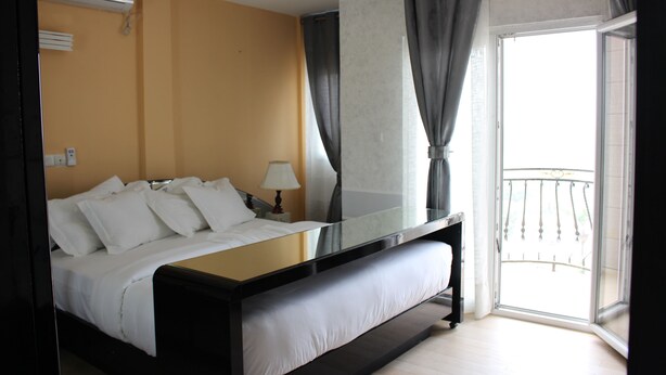 Habitación de hotel con una cama grande, una mesita de noche, una lámpara y vistas al balcón exterior.