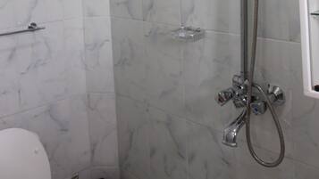 A bathroom with a shower, a toilet, and a marble-tiled wall.