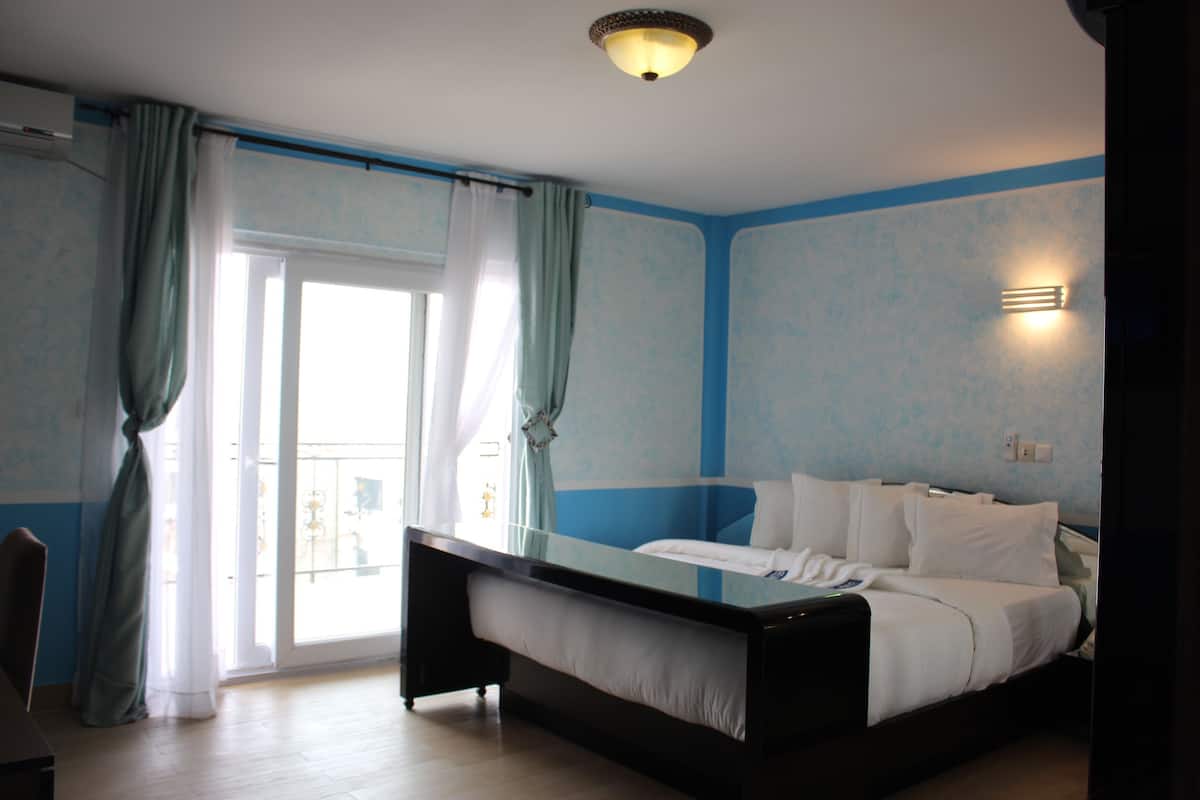 Quarto de hotel com uma cama grande, divisória de vidro e vista para o exterior.