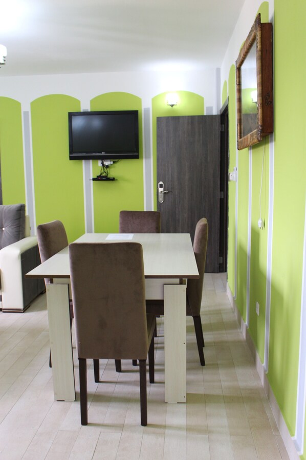 A dining area with a table and chairs, a flat-screen TV mounted on the wall, and a door with a mirror.