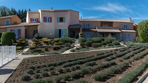 Une rangée de bâtiments de style méditerranéen, avec des toits en tuiles de terre cuite, entourés de jardins bien entretenus et sous un ciel d’un bleu limpide.