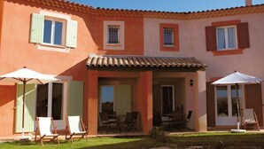 Une maison à deux étages avec un toit en tuiles, une terrasse avec des meubles d’extérieur et un petit jardin.