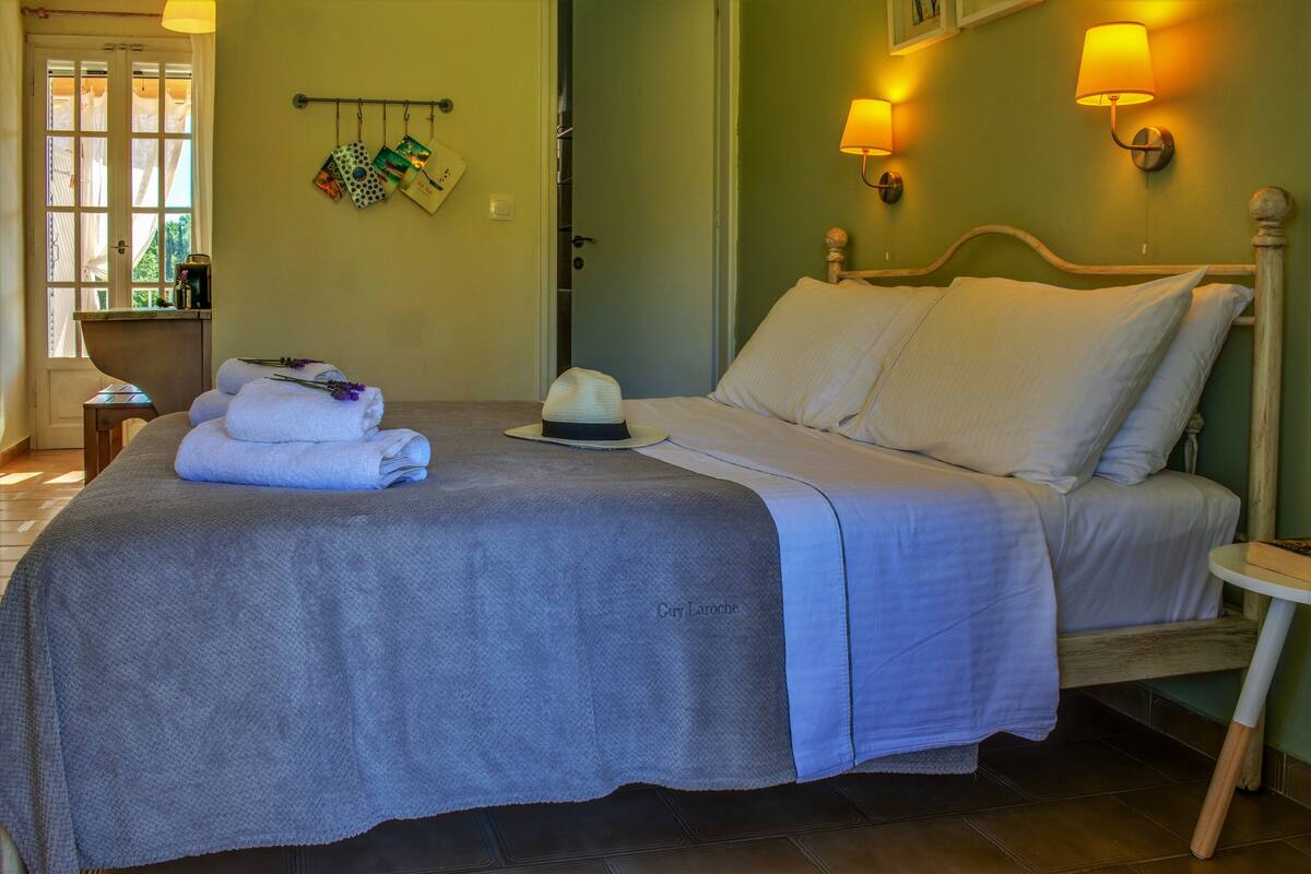 A neatly made bed with a grey blanket, a white pillow, and a hat on the bed. There are two wall-mounted lamps on either side of the bed.
