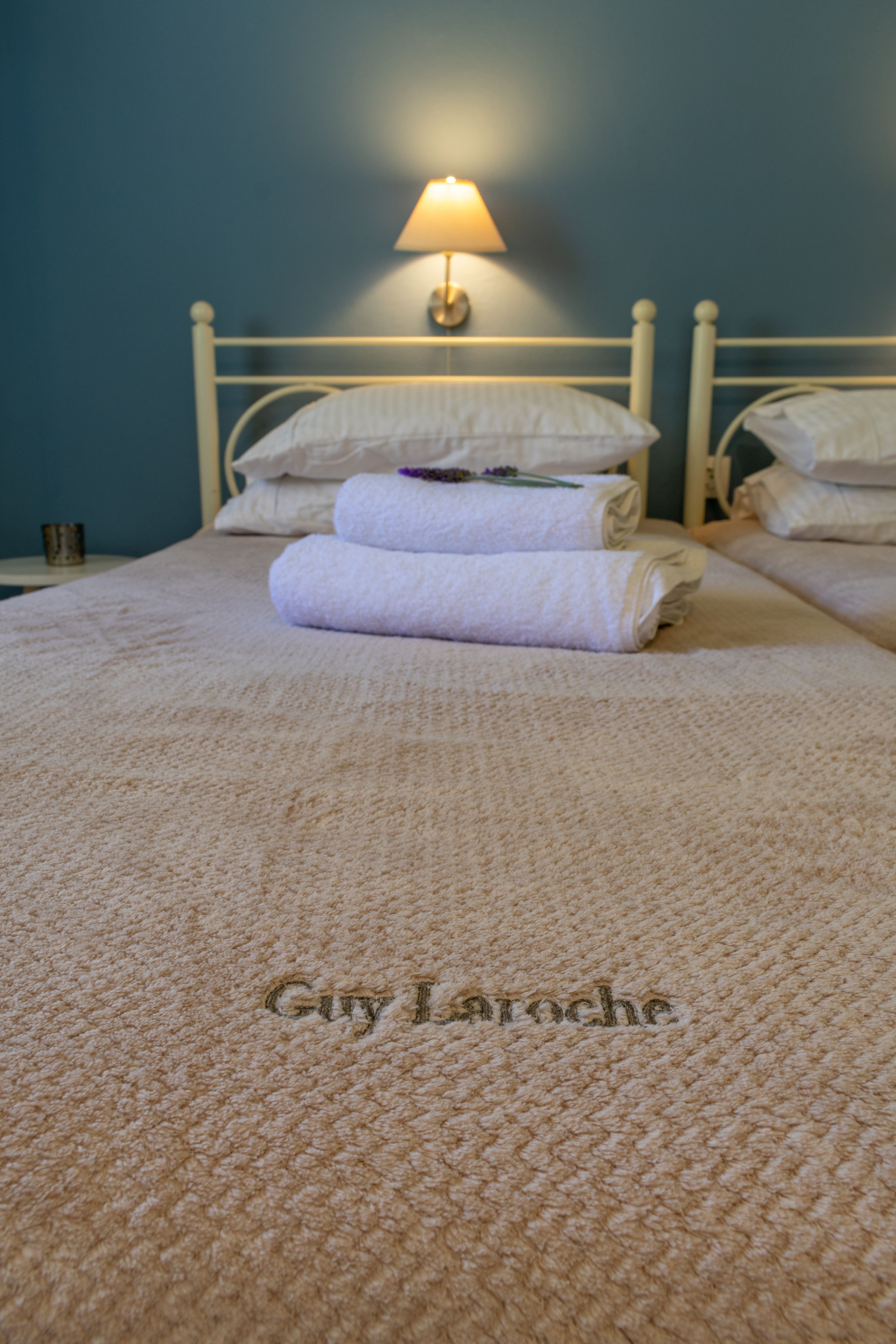 A neatly made bed with a white comforter and pillows, a lamp on the nightstand, and a towel folded on the bed.