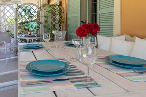A dining table set with blue plates, wine glasses, and a vase with red roses. - Kapella Apartments (Corfu)