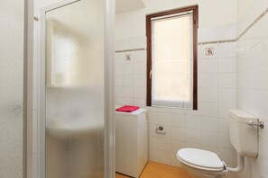 A small bathroom with a toilet, a washing machine, and a window with blinds. - Impero House Rent - Simone (Stresa)