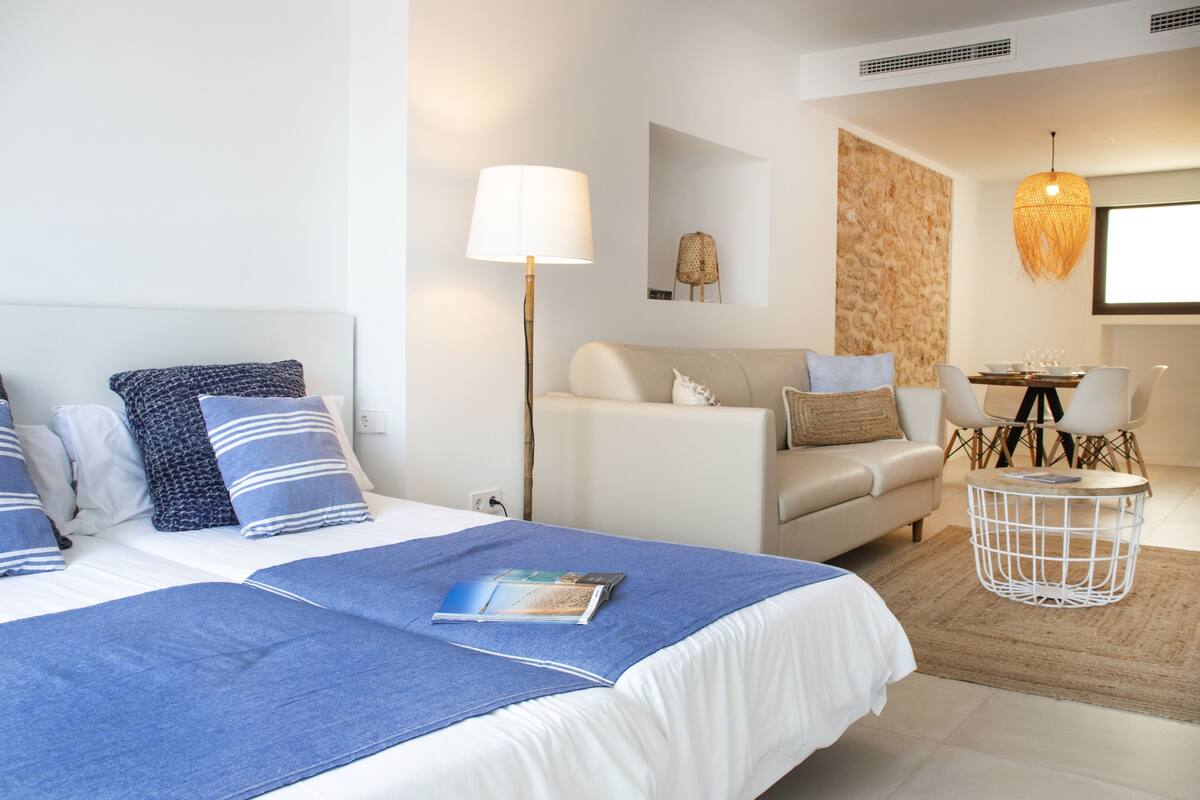 Una habitación de hotel moderna con una cama grande, un sofá, una mesa de comedor y una lámpara colgante.