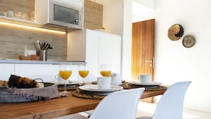 Une cuisine moderne avec des meubles en bois, un four à micro-ondes et un coin repas comprenant des chaises blanches et une table en bois, le tout préparé pour le petit-déjeuner.