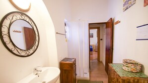 Ein Badezimmer mit einem weißen Waschbecken, einem Holzschrank, einem Spiegel mit Zierrahmen und einer Holztür zu einem anderen Raum.