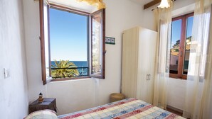 Ein Schlafzimmer mit Bett, einem Fenster mit Meerblick, einem Kleiderschrank und einem kleinen Tisch mit Lampe.