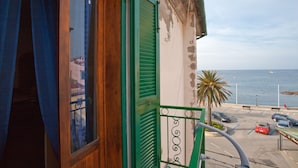 Ein Balkon mit einer Holztür und grünen Fensterläden, der auf einen Parkplatz und das Meer blickt.